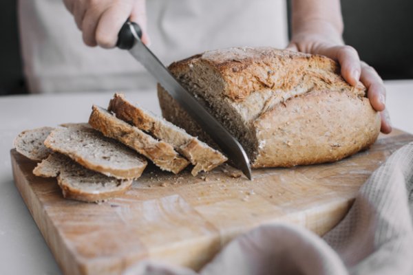 baker-s-hand-slicing-loaf-fresh-bread-with-knife-23-2147955238
